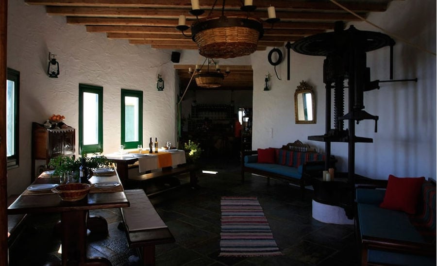 exhibition room with old grape press, wood table with benches and sofa at 'Manalis Winery'
